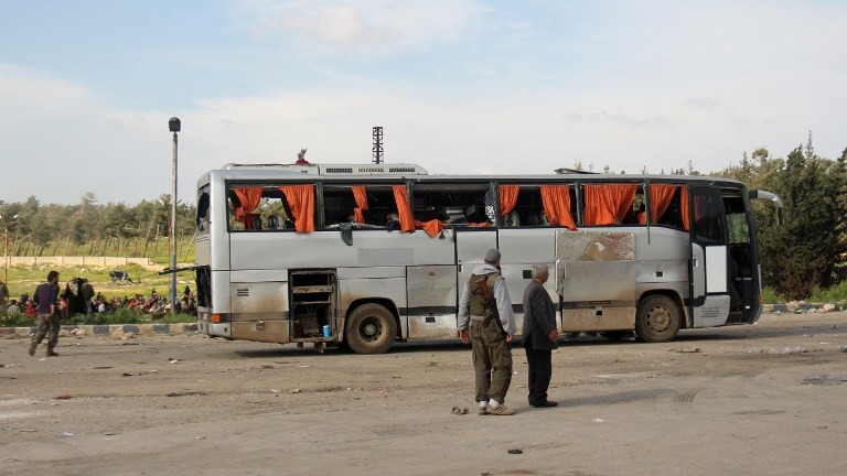 A picture taken on April 15, 2017, shows rebel fighters standing next to a damaged bus following a suicide car bombing in Rashidin, west of Aleppo. (AFP Photo/ Omar Haj Kadour)
