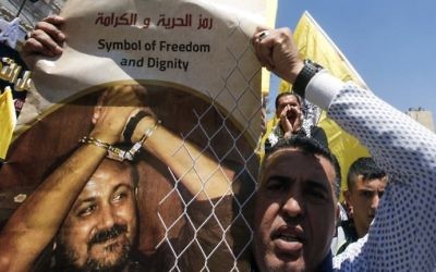 A man holds a photo of Marwan Barghouti calling for his release during a rally supporting Palestinian prisoners detained in Israeli jails in the West Bank city of Hebron on April 17, 2017. (AFP/Hazem Bader)