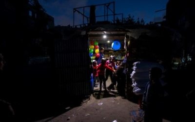 Palestinian children stand at the entrance of a shop lit up using a generator during a power cut in a poor neighborhood of Beit Lahiya, in the northern Gaza Strip, April 17, 2017. (AFP/Mahmud Hams)