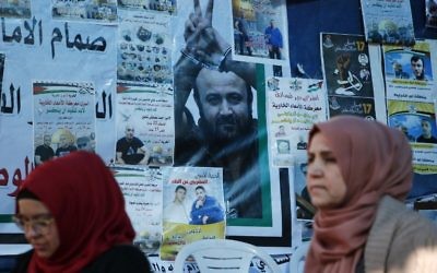 Palestinian women walk past a wall bearing posters, including a portrait of prominent prisoner Marwan Barghouti, during a rally in the West Bank city of Ramallah in support of him and other prisoners on hunger strike in Israeli jails on April 24, 2017. (AFP/Abbas Momani)
