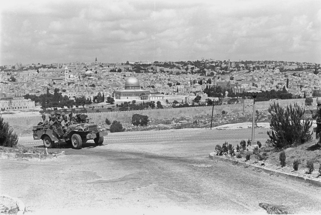 Paratroopers ride in a jeep near the East Jerusalem neighborhood of A-Tur, with the Old City of Jerusalem behind them, on June 5, 1967. (Amos Zucker/Bamahane Magazine/Defense Ministry's IDF Archive)