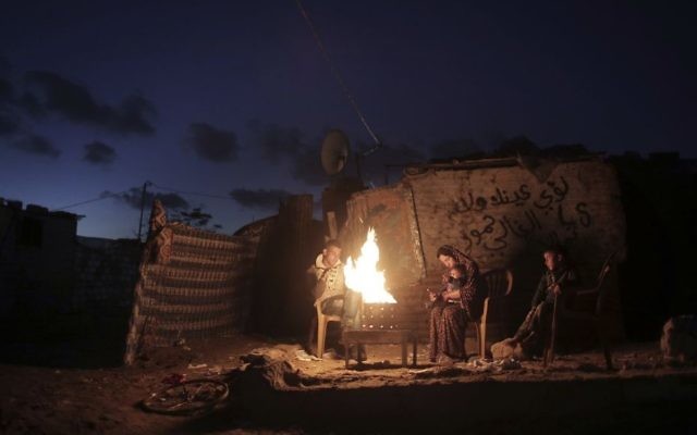 In this Sunday, Jan. 15, 2017 file photo, a Palestinian family warm themselves up with a fire outside their makeshift house during a power cut in a poor neighborhood in town of Khan Younis in the southern Gaza Strip. (AP Photo/ Khalil Hamra, File)