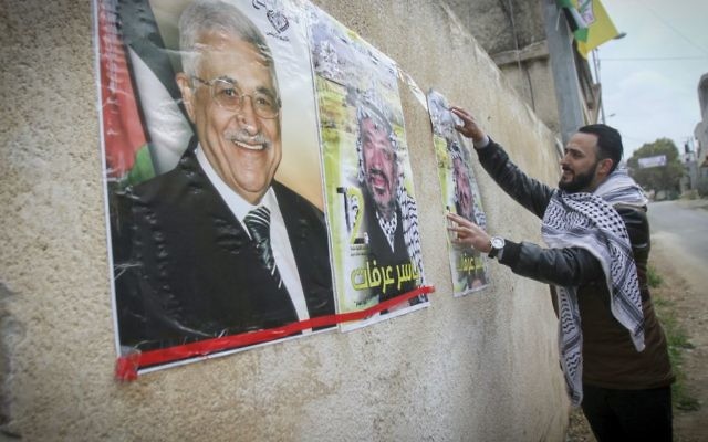 A Palestinian hangs a poster depicting late Palestinian leader Yasser Arafat and Palestinian Authority President Mahmoud Abbas, in the West Bank city of Nablus, March 14, 2017. (Nasser Ishtayeh/Flash90