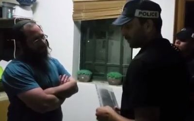 Elkana Pikar (L) speaks with an Israel Police officer from the Judea and Samaria Division who is handing him a restraining order from the West Bank in his home in the Yitzhar settlement on May 16, 2017. (Screen capture/YouTube)