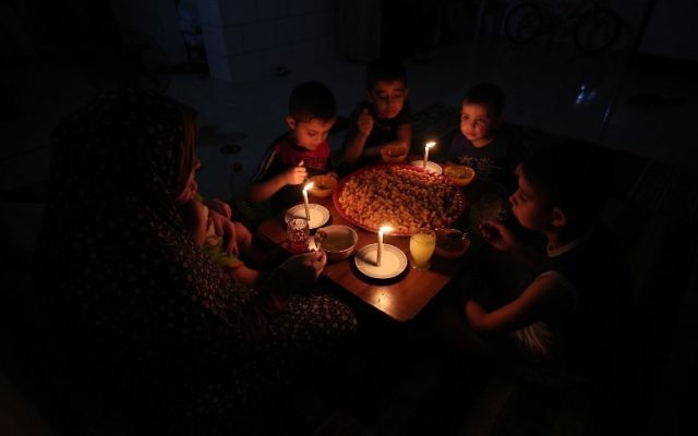 A palestinian family eats dinner by candlelight at their makeshift home in the Rafah refugee camp, in the southern Gaza Strip, during a power outage June 11, 2017. (AFP/SAID KHATIB)