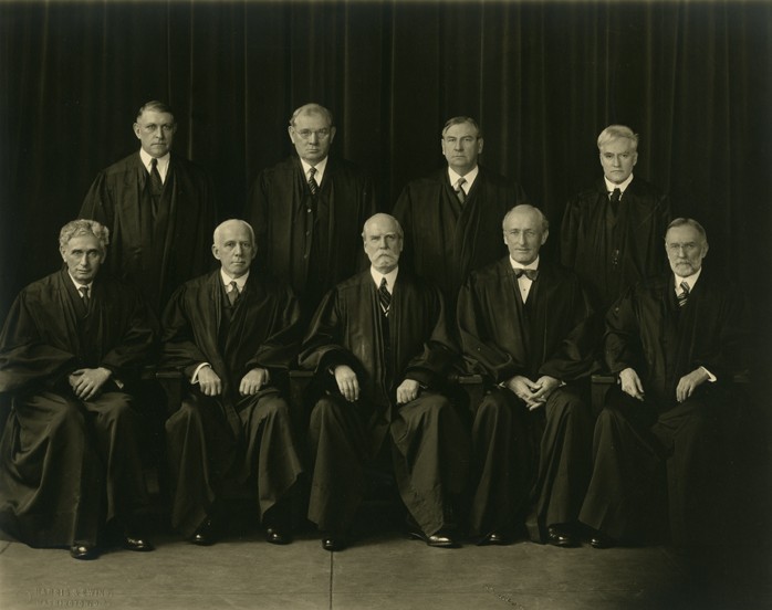 Posed group photograph, justices wearing robes of office. Seated, front row, far left, Louis Dembitz Brandeis; standing, back row, far right is Benjamin Nathan Cardozo. (Harris & Ewing/ Historical & Special Collections, Harvard Law School Library)
