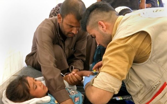 In this screen grab from video, a man comforts his daughter as a doctor treats her after she was taken ill with suspected food poisoning in the Hassan Sham U2 camp for displaced people east of Mosul, Iraq, June 13, 2017. (AP/Balint Szlanko)