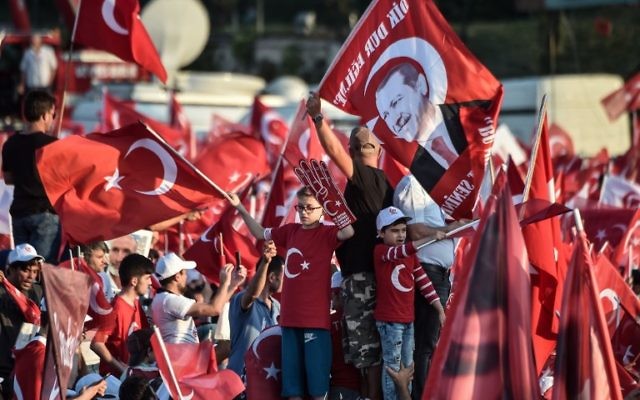 People wave Turkish national flags as they stand near the "July 15 Martyrs Bridge" (Bosphorus Bridge) in Istanbul on July 15, 2017.(AFP PHOTO / OZAN KOSE)