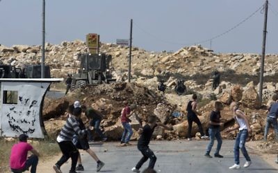 Illustrative: Palestinian protesters throw rocks at Israeli soldiers in the West Bank village of Kobar, while an army bulldozer closes the main road to the area during an operation to prepare the home of a terrorist for demolition on July 22, 2017. (AP Photo/Nasser Nasser)
