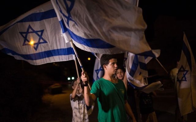 Young Jewish teens wave Israeli flags outside the Salomon home in the Halamish settlement in the northern West Bank on July 22, 2017. (Hadas Parush/FLASH90)
