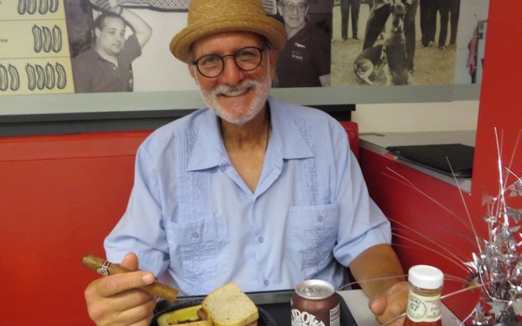Alan Gross with some of his favorite things — a pastrami sandwich and a Cuban cigar — at Loeb’s Deli in Washington DC, July 12, 2017. (Ron Kampeas)