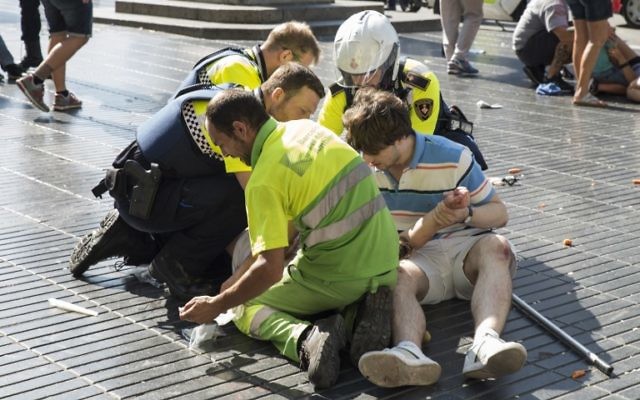 A person is helped by Spanish policemen and two men after a van ploughed into the crowd, killing at least 13 people and injuring around 100 others on the Rambla in Barcelona on August 17, 2017. (AFP PHOTO / Nicolas CARVALHO OCHOA)