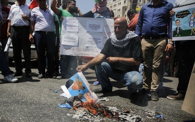 A picture taken on August 24, 2017 in the West Bank city of Ramallah shows a Palestinian holding a burnt flyer depicting US President Donald J. Trump defaced with cartoon shoes on his head, during a protest against the arrival of a US delegation headed by Senior White House Advisor Jared Kushner to meet with Palestinian Authority President Mahmoud Abbas. / AFP PHOTO / ABBAS MOMANI