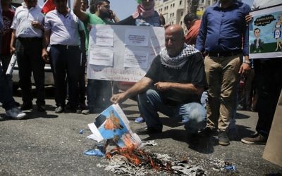 A picture taken on August 24, 2017 in the West Bank city of Ramallah shows a Palestinian holding a burnt flyer depicting US President Donald J. Trump defaced with cartoon shoes on his head, during a protest against the arrival of a US delegation headed by Senior White House Advisor Jared Kushner to meet with Palestinian president Mahmoud Abbas. (AFP PHOTO / ABBAS MOMANI)