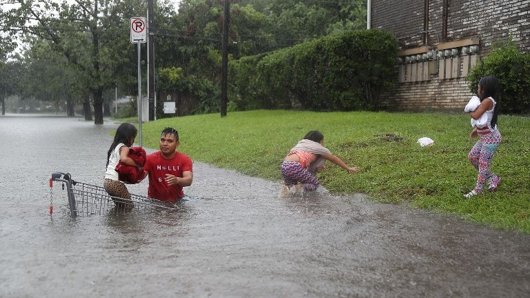 A man helps children across a flooded street as they evacuate their home in Houston August 27, 2017. (Joe Raedle/Getty Images/AFP)
