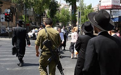 Illustrative: Ultra-Orthodox Jewish men in the Mea Shearim neighborhood in Jerusalem walk alongside an Israeli soldier. June 6, 2008. (Lara Savage/Flash 90)