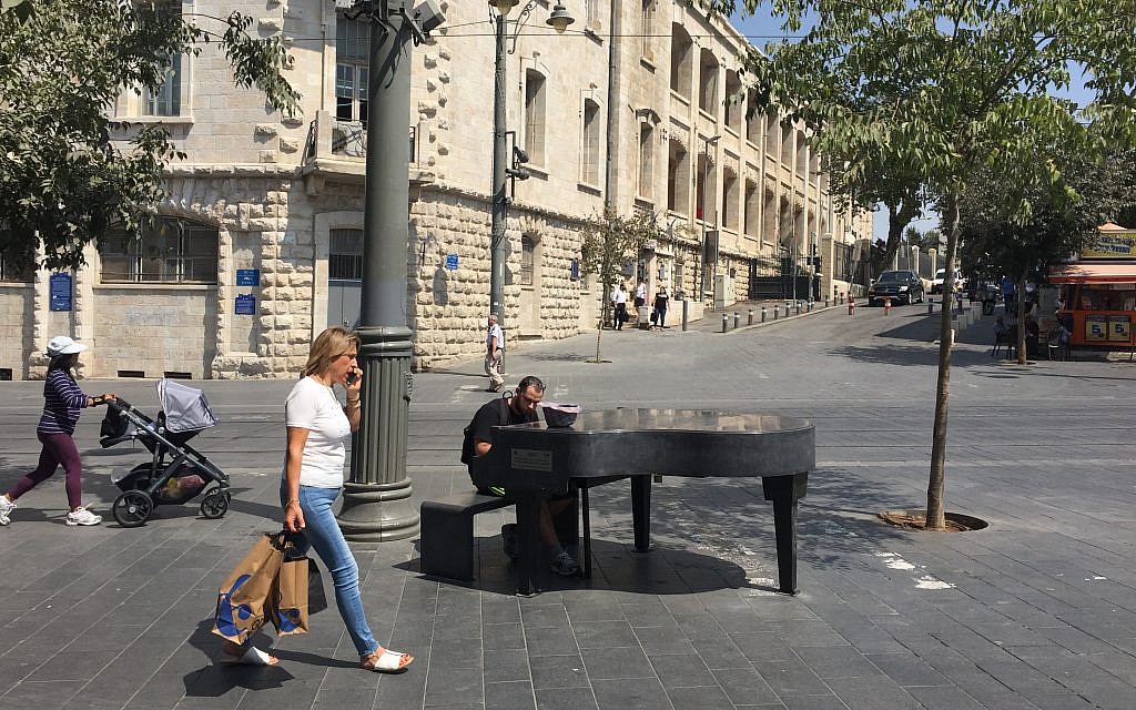 Passersby and a pianist at the Cadenza Piano temporarily installed at a busy crossroads in downtown Jerusalem, bringing music to the public (Jessica Steinberg/Times of Israel)