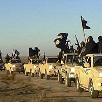 In this undated file photo, militants of the Islamic State group hold up their weapons and wave its flags on their vehicles in a convoy to Iraq, in Raqqa, Syria. (Militant website via AP, File)