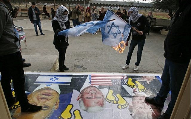 Palestinians burn Israeli flags next to a poster bearing images of US President Donald Trump (R), US Vice President Mike Pence (C), and Prime Minister Benjamin Netanyahu, during a demonstration at the al-Quds Open University in Dura, a village on the outskirts of the West Bank city of Hebron, on December 13, 2017.(AFP Photo/Hazem Bader)