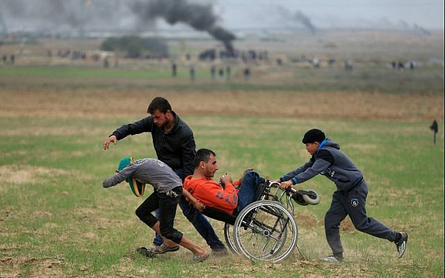 Palestinians assist a demonstrator in a wheelchair during clashes with Israeli security forces near the border fence east of Gaza City on December 22, 2017. (AFP Photo/Mohammed Abed)