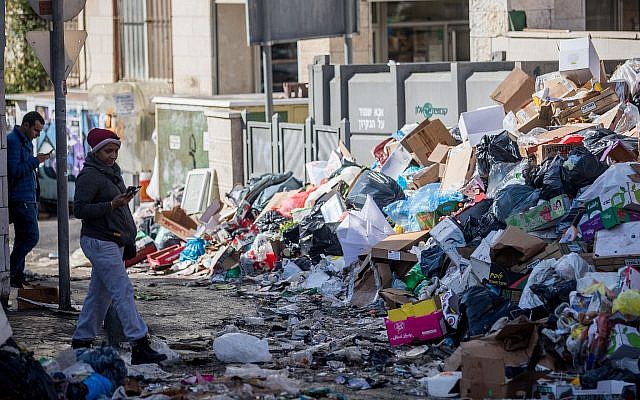 Shoppers walk past piles of garbage left by striking city workers, at Jerusalem's Mahane Yehuda Market, on January 7, 2018. (Yonatan Sindel/Flash90)