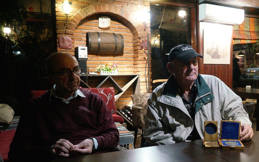 Rexhep Hoxha, left, and Fatos Qoqja in a bar in Tirania, Albania, November 8, 2017. Qoqja is pictured with a medal that his father received for saving Jews during the Holocaust. (Cnaan Liphshiz/via JTA)