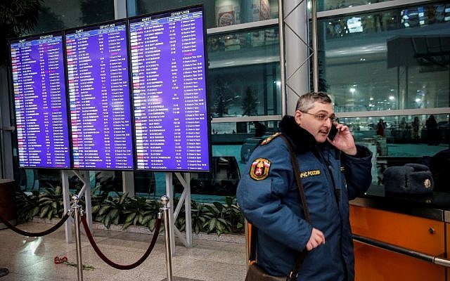 A Russian emergency employee stands next to flowers, in tribute to a plane crash victims, placed under of the flight schedule timetables at the Domodedovo International Airport, outside Moscow, February 11, 2018. (Maxim ZMEYEV/AFP)