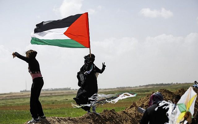 A Palestinian woman wearing niqab (full face veil) flashes the victory gesture while holding a Palestinian flag as others fly kites during a demonstration ahead of Land Day, at a tent city near the border with Israel east of Gaza City on March 29, 2018. (AFP PHOTO / MOHAMMED ABED)