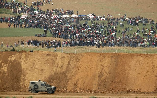 A picture taken on March 30, 2018 from the southern Israeli kibbutz of Nahal Oz across the border from the Gaza strip shows Palestinians participating in a protests, with Israeli military vehicles seen below in the foreground. (AFP PHOTO / Jack GUEZ)