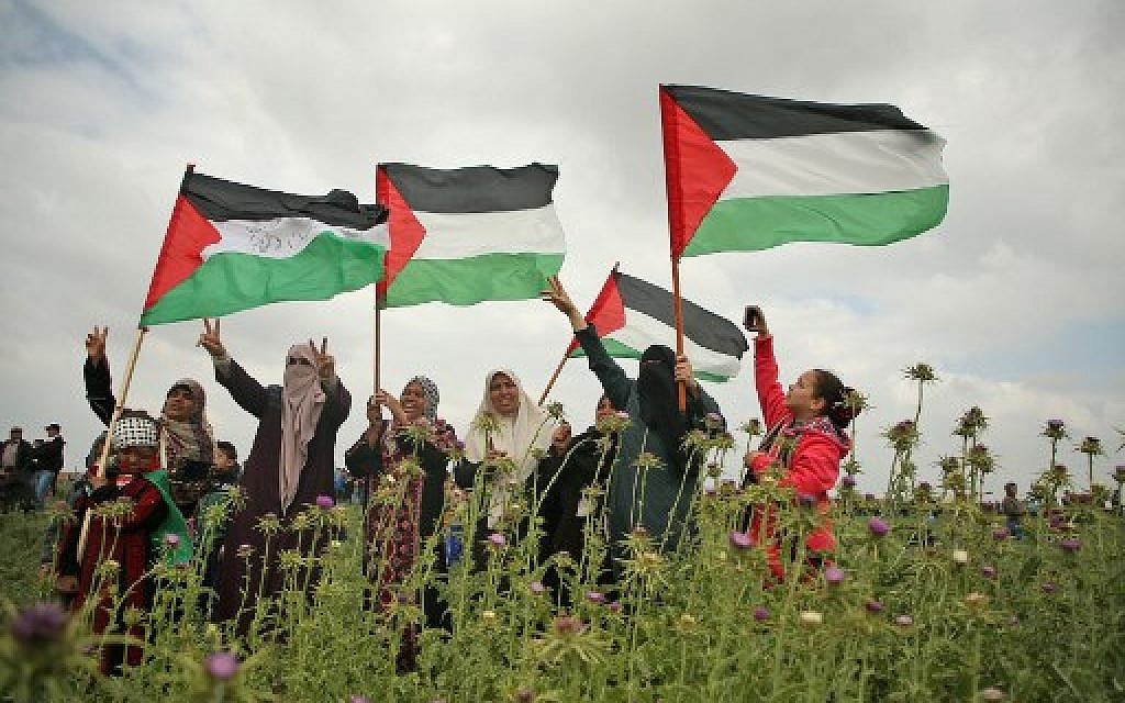 Palestinian women wave Palestinian flags and flash the victory gesture during a protest near the border with Israel east of Jabalia in the Gaza strip on March 30, 2018. (AFP PHOTO / Mohammed ABED)