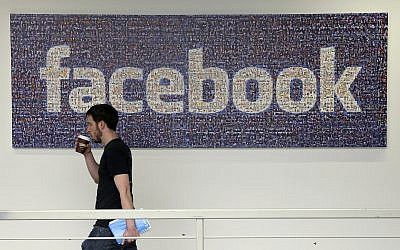 In this March 15, 2013, file photo, a Facebook employee walks past a sign at Facebook headquarters in Menlo Park, Calif.  (AP Photo/Jeff Chiu)