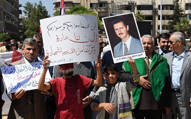 Syrians wave the national flag and wave portraits of President Bashar al-Assad as they gather in Aleppo's Saadallah al-Jabiri square on April 14, 2018, to condemn the strikes carried out by the United States, Britain and France against the Syrian regime. (AFP PHOTO / George OURFALIAN)