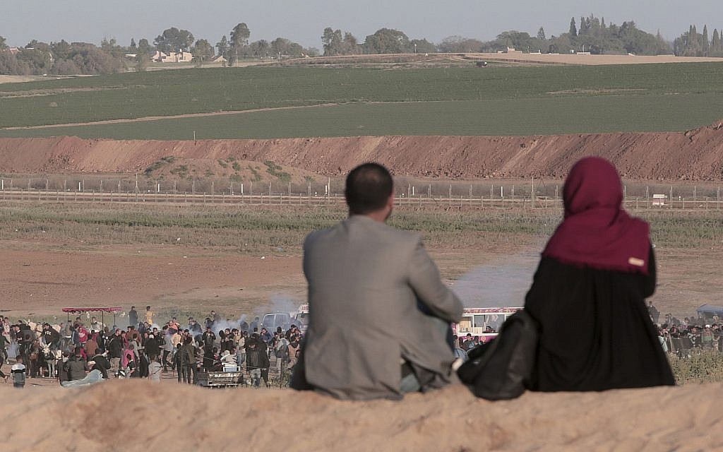 A Palestinian couple sits on a hill as Israeli soldiers fire tear gas at protesters during clashes with  troops along the Gaza Strip border with Israel on March 31, 2018. (AP /Adel Hana)