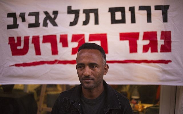 In this Tuesday, April 3, 2018 photo, Eritrean Halofom Sulta sits under a banner "South Tel Aviv against deportation" after speaking to the Associated Press in southern Tel Aviv. (AP Photo/Ariel Schalit)