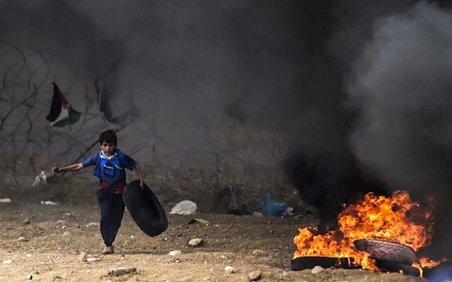 A Palestinian boy protester runs carrying a tire towards a fire during clashes with Israeli forces along the border with the Gaza strip east of Gaza City on May 4, 2018 (AFP PHOTO / MAHMUD HAMS)