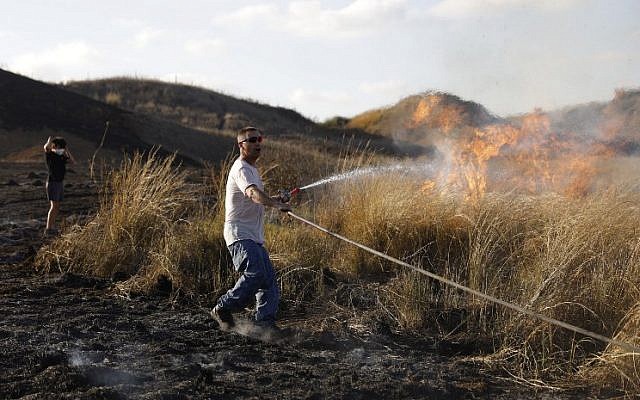 An Israeli man extinguishes a fire in a field next to Kibbutz Be’eri reportedly caused by flaming kites flown into Israel from the Gaza Strip on June 18, 2018. (AFP Photo/Menahem Kahana)