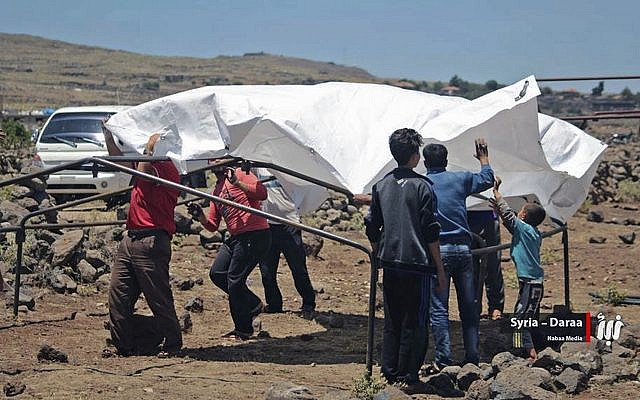 This June 22, 2018 photo provided by Nabaa Media, a Syrian opposition media outlet, shows people who fled from Daraa setting up a tent in the village of Bregia, near the Syria-Israel border, southern Syria. (Nabaa Media, via AP)
