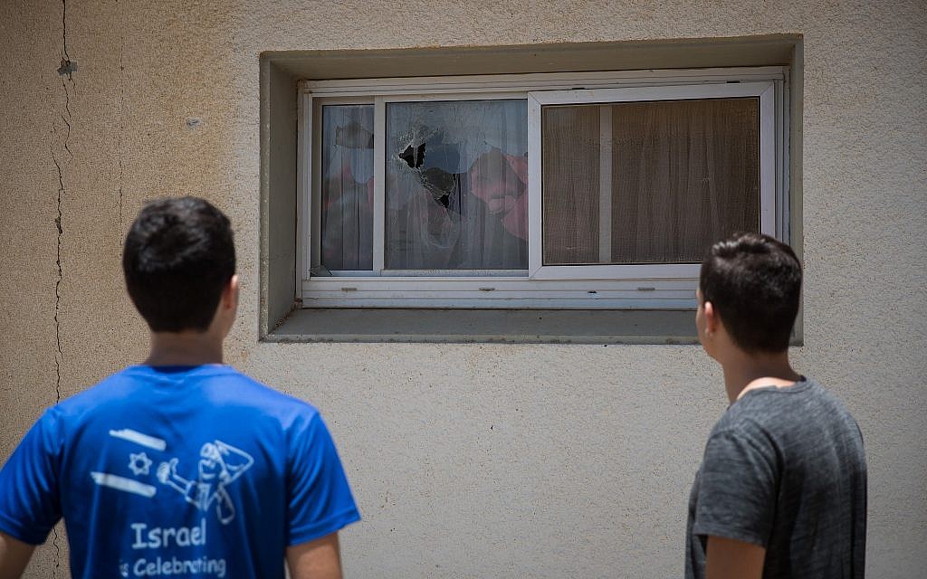 Israelis at a kibbutz near Gaza inspect the scene where a rocket fired from the Strip fell near houses, smashing windows, on June 20, 2018. (Yonatan Sindel/Flash90)