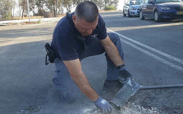 Un sapeur de la police manipule une roquette tirée de Gaza qui a atterri dans une rue de l'une des communautés de la région d'Eshkol le 20 juin 2018. (Police d'Israël) Un sapeur de la police manipule une roquette tirée de Gaza qui a atterri dans une rue de l'une des communautés de la région d'Eshkol le 20 juin 2018. (Police d'Israël)