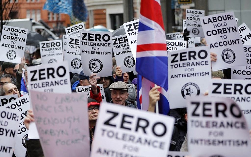 Illustrative: People hold up placards and Union flags as they gather for a demonstration organized by the Campaign Against Anti-Semitism outside the head office of the British opposition Labour Party in central London on April 8, 2018. (AFP/Tolga Akmen)