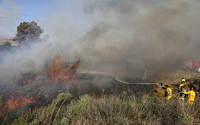 Illustrative: Firefighters extinguish a blaze near the southern city of Sderot caused by an incendiary balloon launched from the Gaza Strip on July 31, 2018. (AFP Photo/Menahem Kahana)
