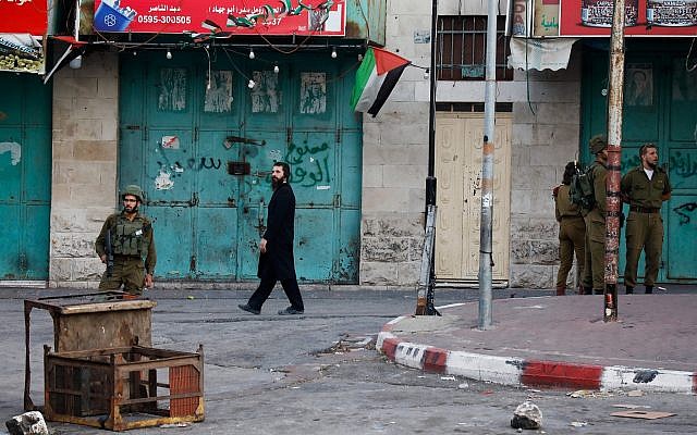 Soldiers guard as an ultra-Orthodox man walks by in the West Bank city of Hebron on July 22, 2018. (Wisam Hashlamoun/Flash90)