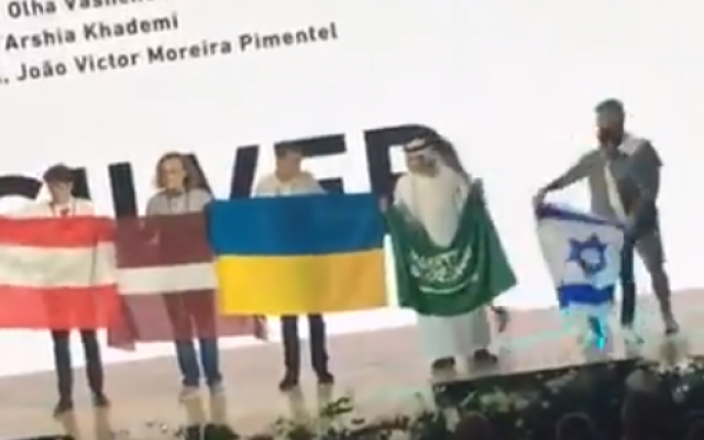 Saudi student Badr al-Mulhim (2R) is seen folding his flag and preparing to move away as Israeli student Raz Lotan (R) comes on stage with an Israeli flag, at the 50th International Chemistry Olympiad in Slovakia and the Czech Republic, in a video that went online on July 29, 2018. (Screenshot: Twitter)