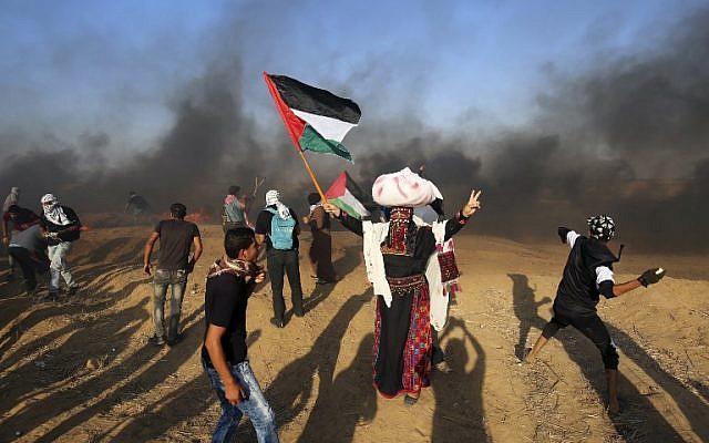 Palestinian protesters throw stones at Israeli forces as a man waves the national flag during a demonstration at the Israel-Gaza border, east of Khan Yunis in the southern Gaza Strip on August 24, 2018. (AFP PHOTO / SAID KHATIB)