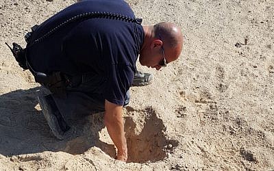 A police officer inspects a crater caused by a rocket fired from the Gaza Strip that struck an open field north of the city of Beersheba on August 9, 2018. (Israel Police)
