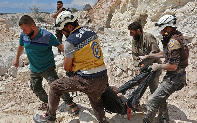 This picture taken in Kafr Ain on September 7, 2018, shows members of the Syrian Civil Defence, also known as the 'White Helmets,' carrying a victim after airstrikes, four kilometers east of Khan Shaykhun in the southern countryside of Idlib province (AFP PHOTO / Anas AL-DYAB)
