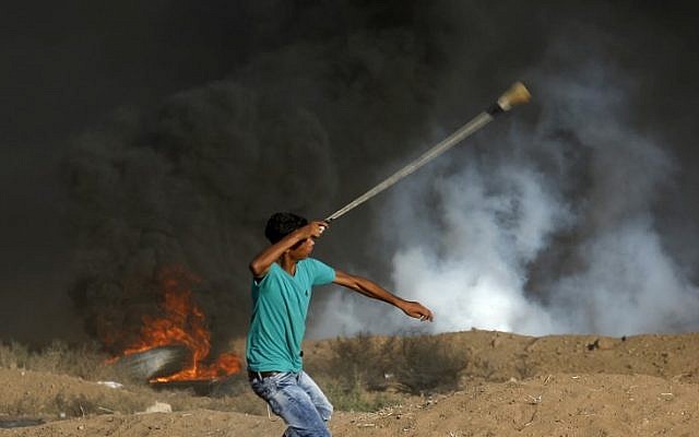 Illustrative: A Palestinian protester uses a slingshot to throw stone toward Israeli forces firing tear gas during a demonstration along the border fence east of Gaza City on September 14, 2018. (AFP/Said Khatib)