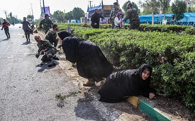 This picture taken on September 22, 2018 in the southwestern Iranian city of Ahvaz shows Iranian women and soldiers taking cover next to bushes at the scene of an attack on a military parade in the southwestern Khuzestan province on September 22, 2018. (AFP/ ISNA / MORTEZA JABERIAN)