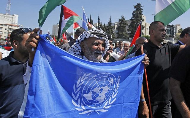 Palestinian protesters wave UN and national flags in front of a fabiricated giant refugee card of their President Mahmud Abbas, during a protest against the US decision earlier this year to cut funds to UN aid to Palestinians,  in  the West Bank city of Bethlehem, on September 26, 2018.  (AFP/Musa Al SHAER)