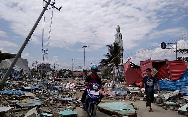Residents make their way along a street full of debris after an earthquake and tsunami hit Palu, on Sulawesi island on September 29, 2018. Rescuers scrambled to reach tsunami-hit central Indonesia and assess the damage after a strong quake brought down several buildings and sent locals fleeing their homes for higher ground. / AFP PHOTO / MUHAMMAD RIFKI